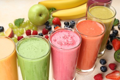 Photo of Fresh colorful fruit smoothies and ingredients on beige table, closeup