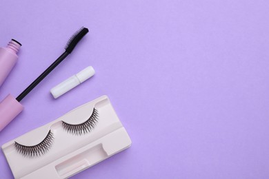 Flat lay composition with fake eyelashes and mascara brush on lilac background. Space for text