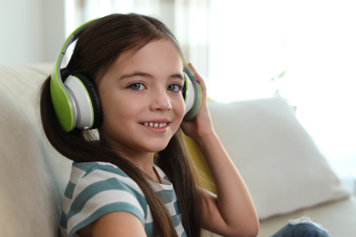 Cute little girl with headphones listening to audiobook at home
