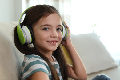 Photo of Cute little girl with headphones listening to audiobook at home