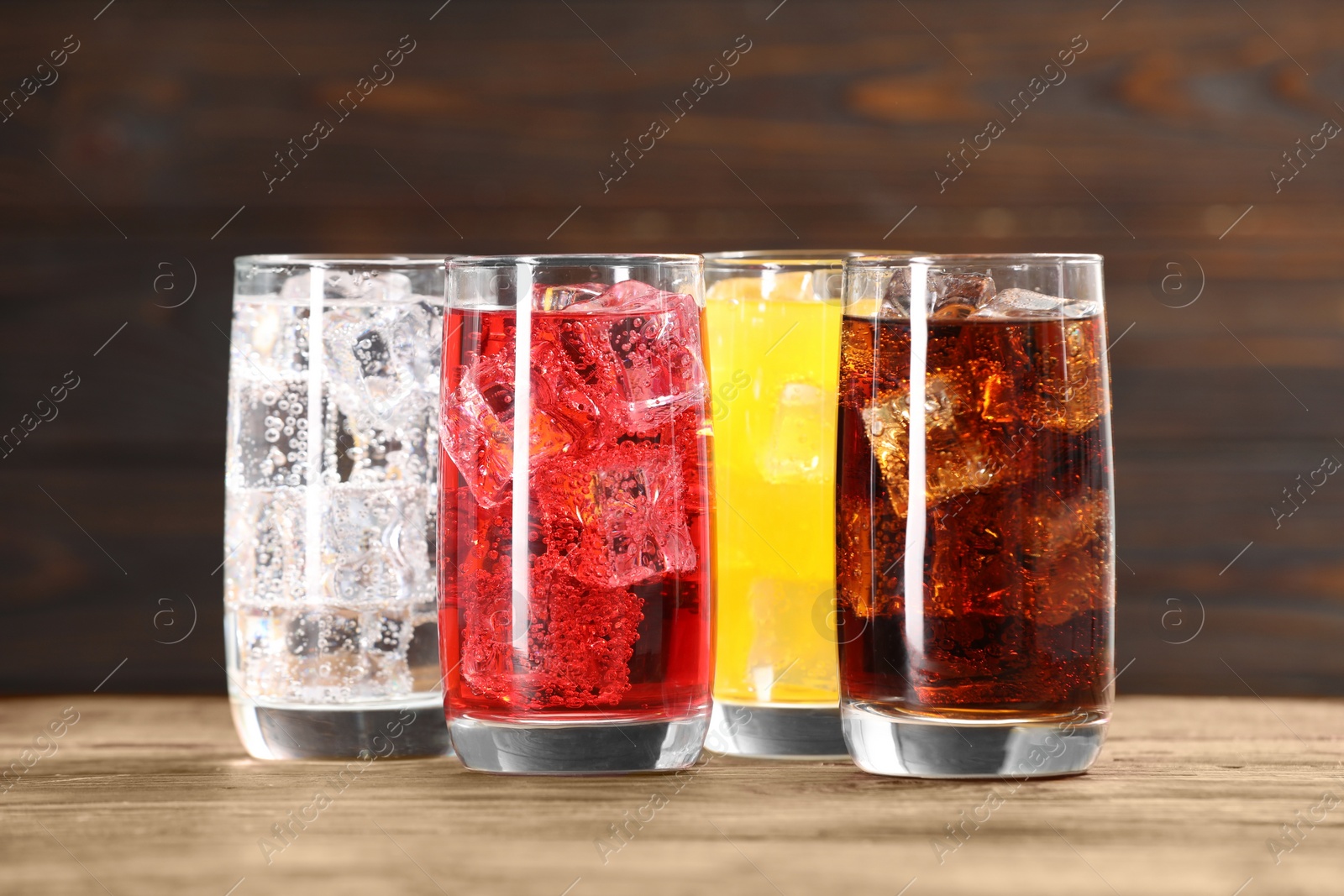 Photo of Glasses of different refreshing soda water with ice cubes on wooden table