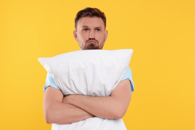 Photo of Unhappy man with pillow on yellow background. Insomnia problem