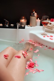 Photo of Woman taking bath with rose petals, closeup. Romantic atmosphere