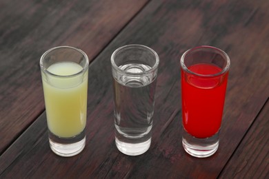 Photo of Shots with lime juice, tequila and sangria as colors of mexican flag on wooden table. Traditional serving