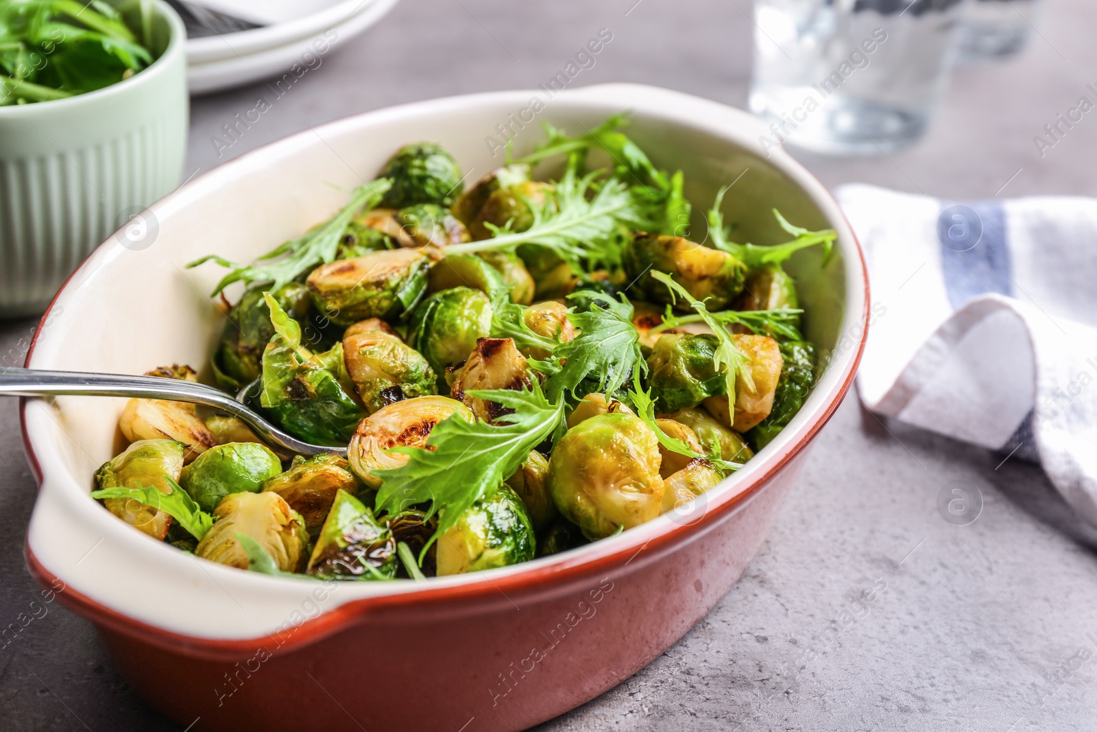 Photo of Roasted Brussels sprouts with arugula in baking dish on grey table, closeup