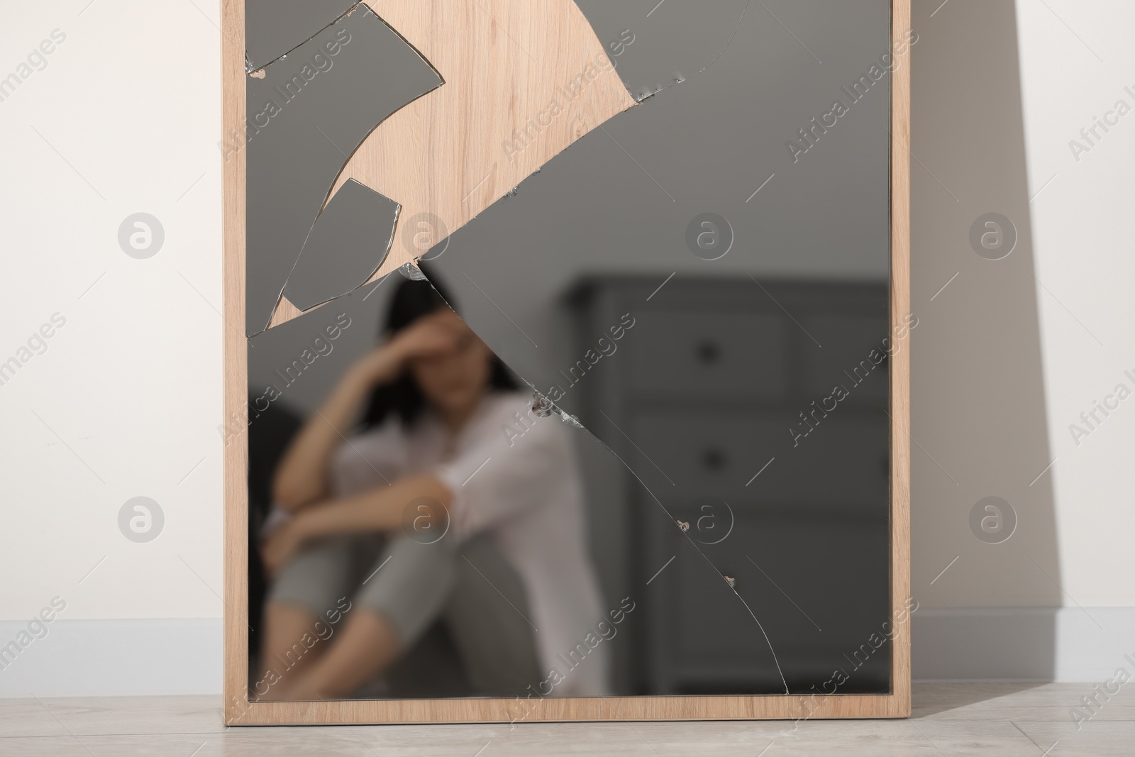 Photo of Mental problems. Blurred reflection of depressed woman in broken mirror indoors