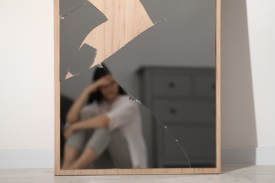 Photo of Mental problems. Blurred reflectiondepressed woman in broken mirror indoors
