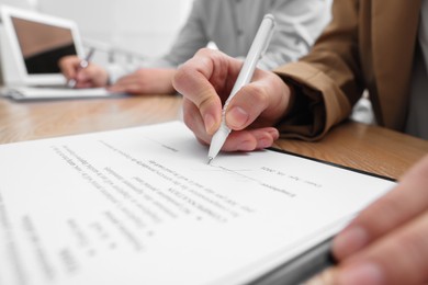 Photo of Woman signing contract at table in office, closeup.