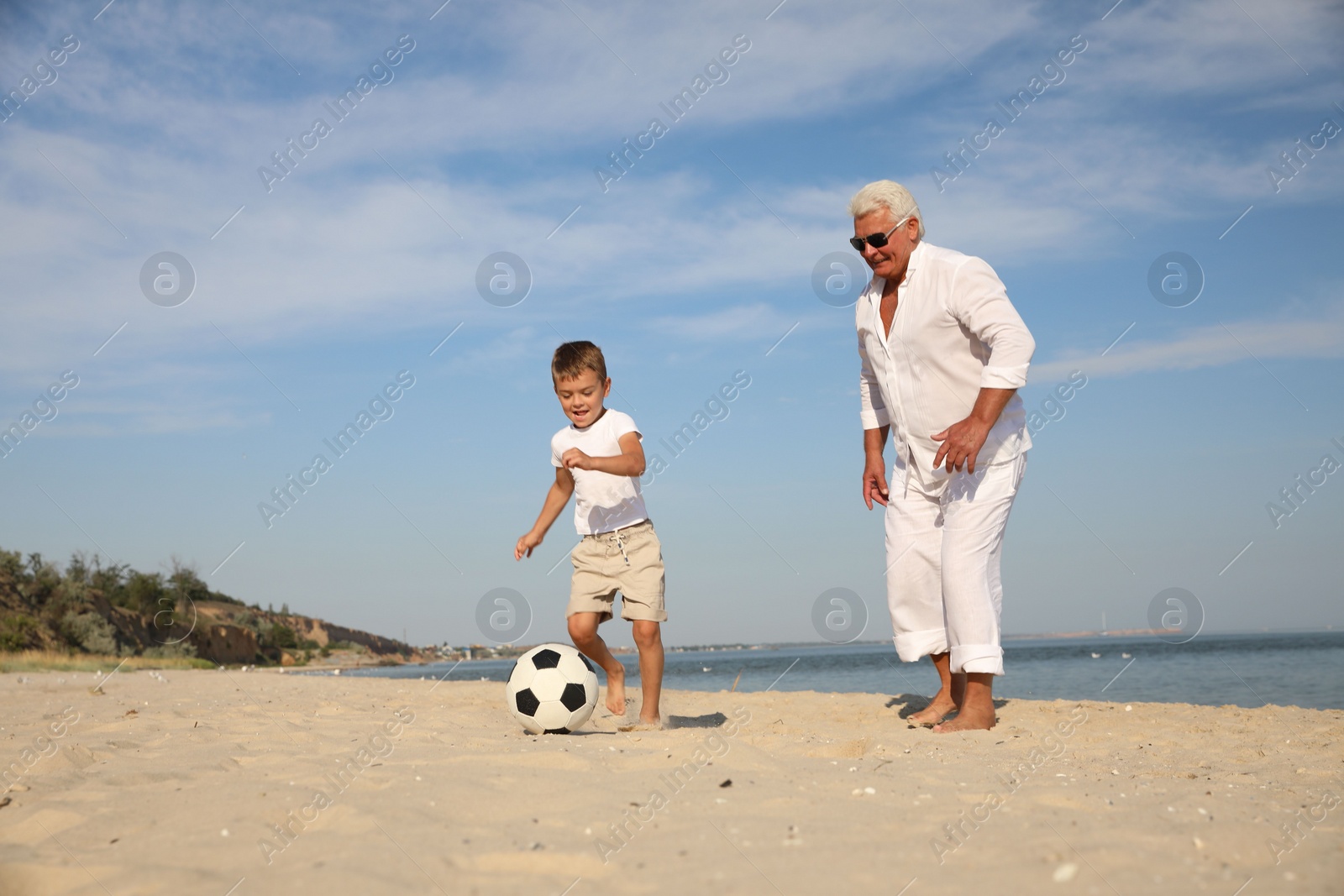 Photo of Cute little boy and grandfather playing with soccer ball on sea beach