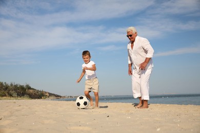 Cute little boy and grandfather playing with soccer ball on sea beach