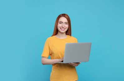 Smiling young woman working with laptop on light blue background