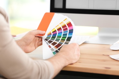 Photo of Designer with paint color palette samples at table, closeup