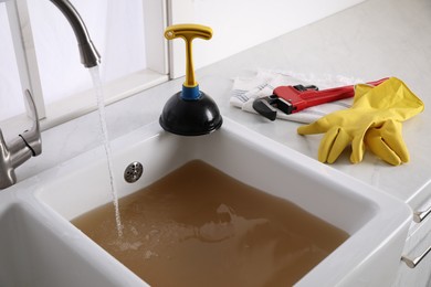 Photo of Kitchen counter with clogged sink, plunger and plumber's accessories