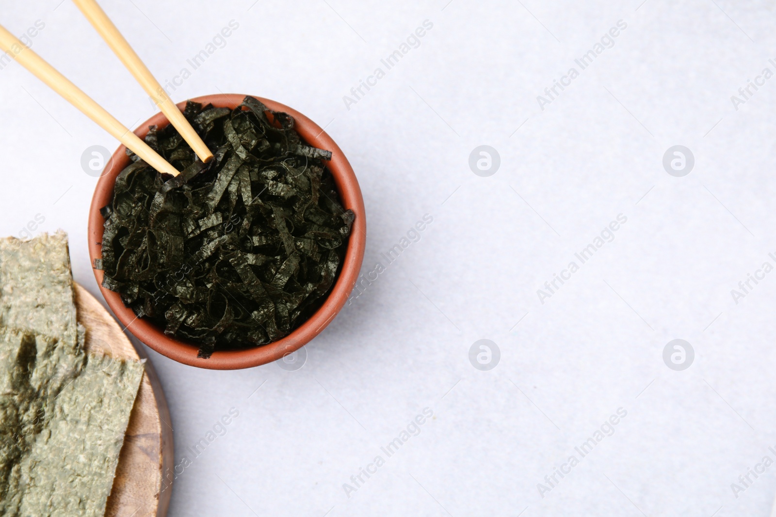 Photo of Bowl with chopped nori sheets and chopsticks on white table, flat lay. Space for text