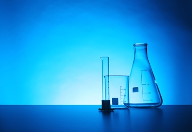 Photo of Empty chemistry laboratory glassware on table against color background