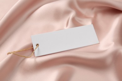 Photo of Blank white tag on pink silky fabric, closeup. Space or text