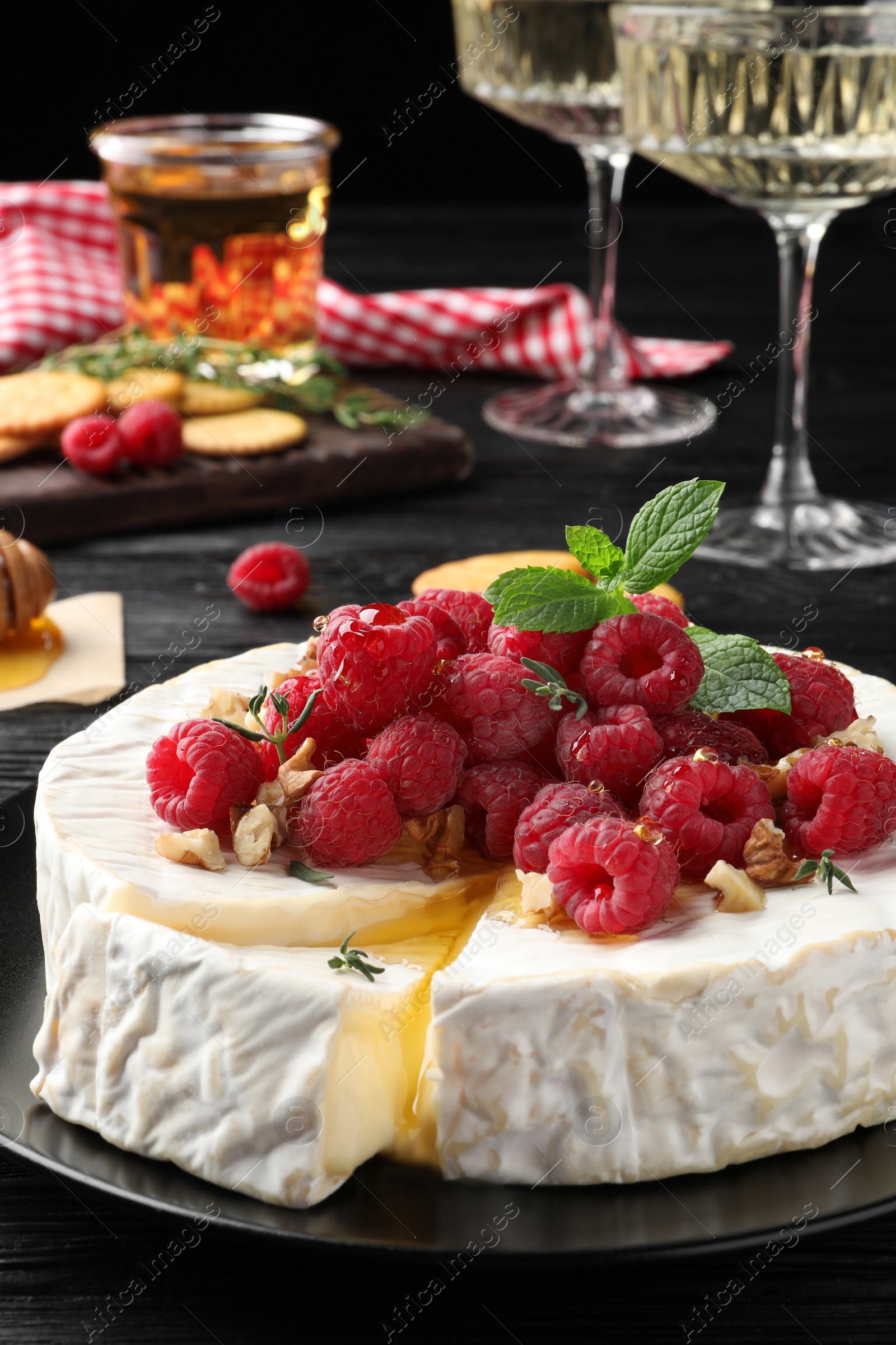 Photo of Brie cheese served with raspberries and walnuts on black plate, closeup