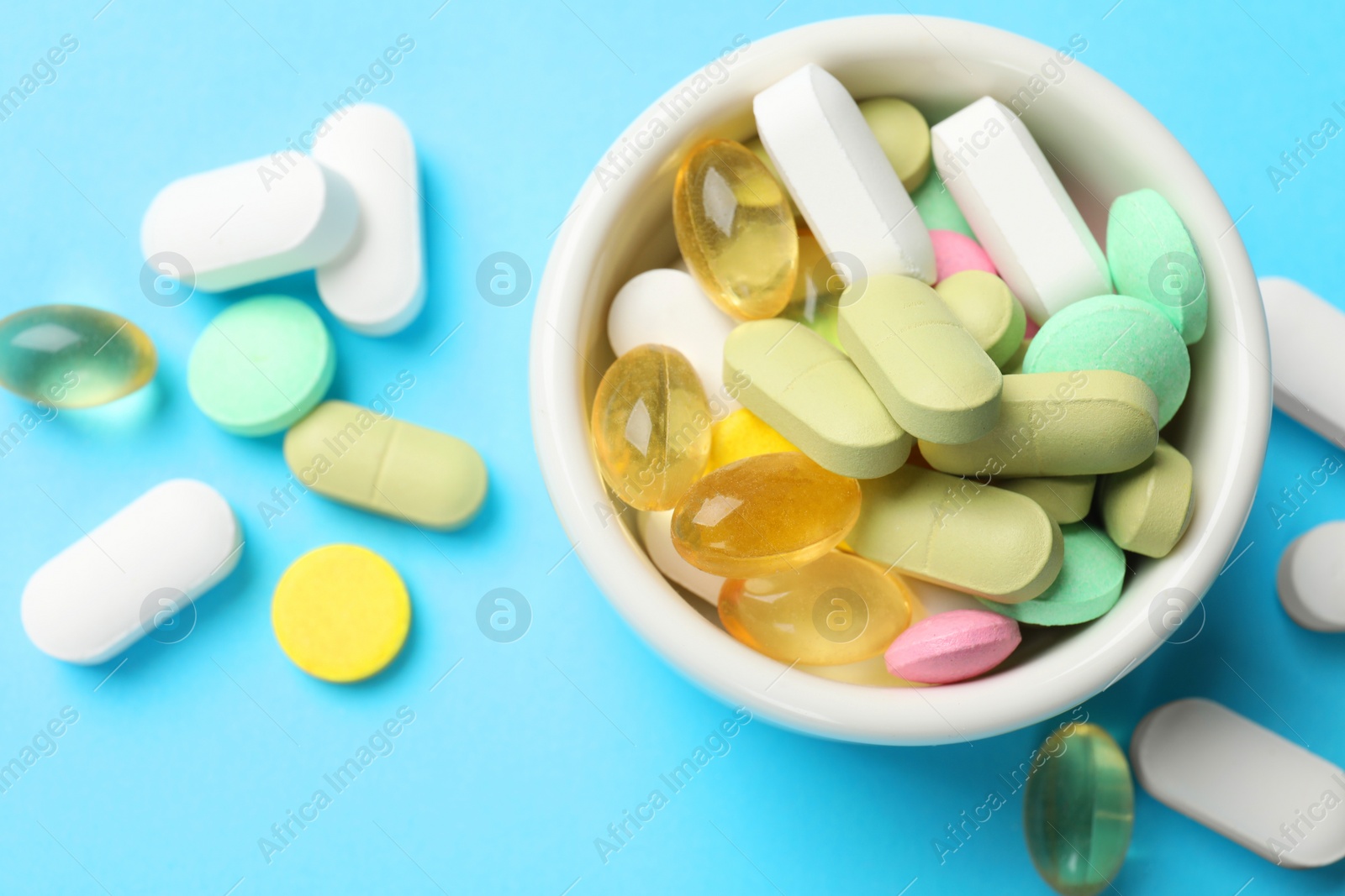 Photo of Different vitamin pills in bowl on light blue background, top view