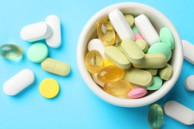 Photo of Different vitamin pills in bowl on light blue background, top view