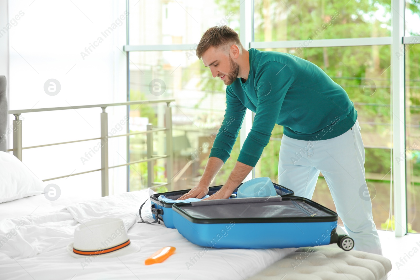 Photo of Young man packing suitcase for summer journey on bed