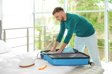 Photo of Young man packing suitcase for summer journey on bed