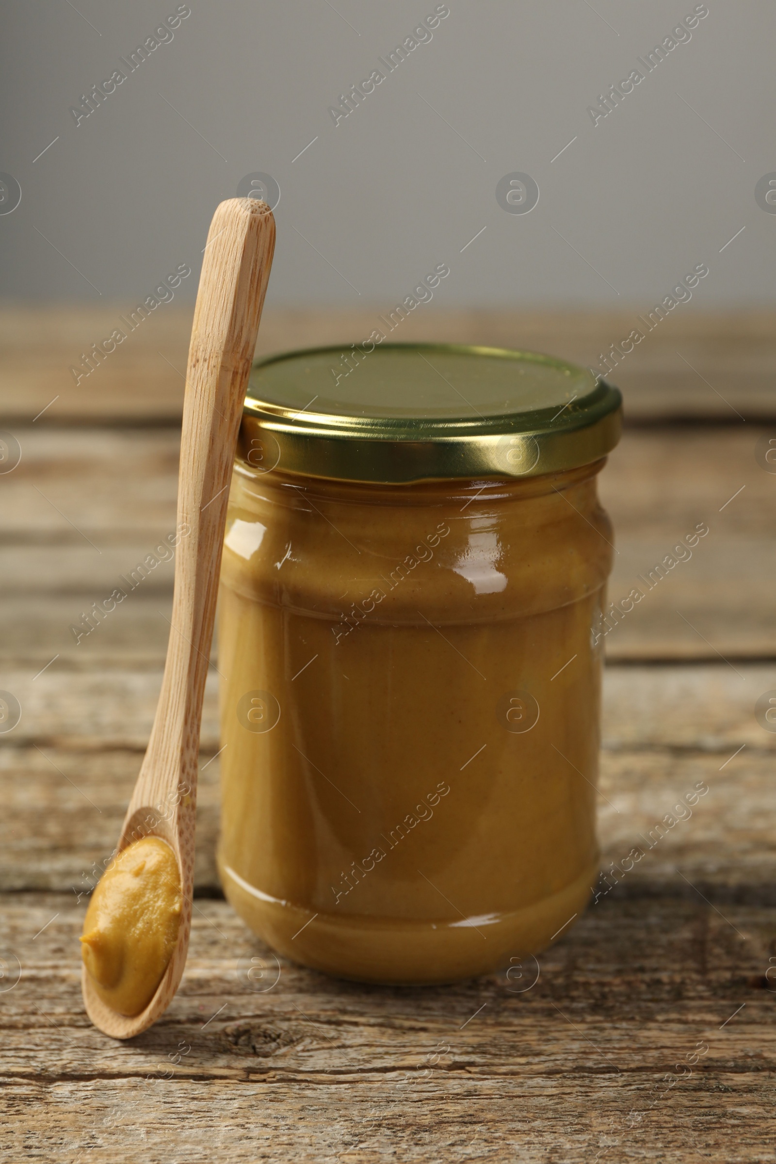 Photo of Jar and spoon with tasty mustard sauce on wooden table, closeup