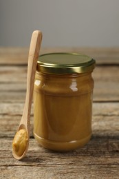 Photo of Jar and spoon with tasty mustard sauce on wooden table, closeup