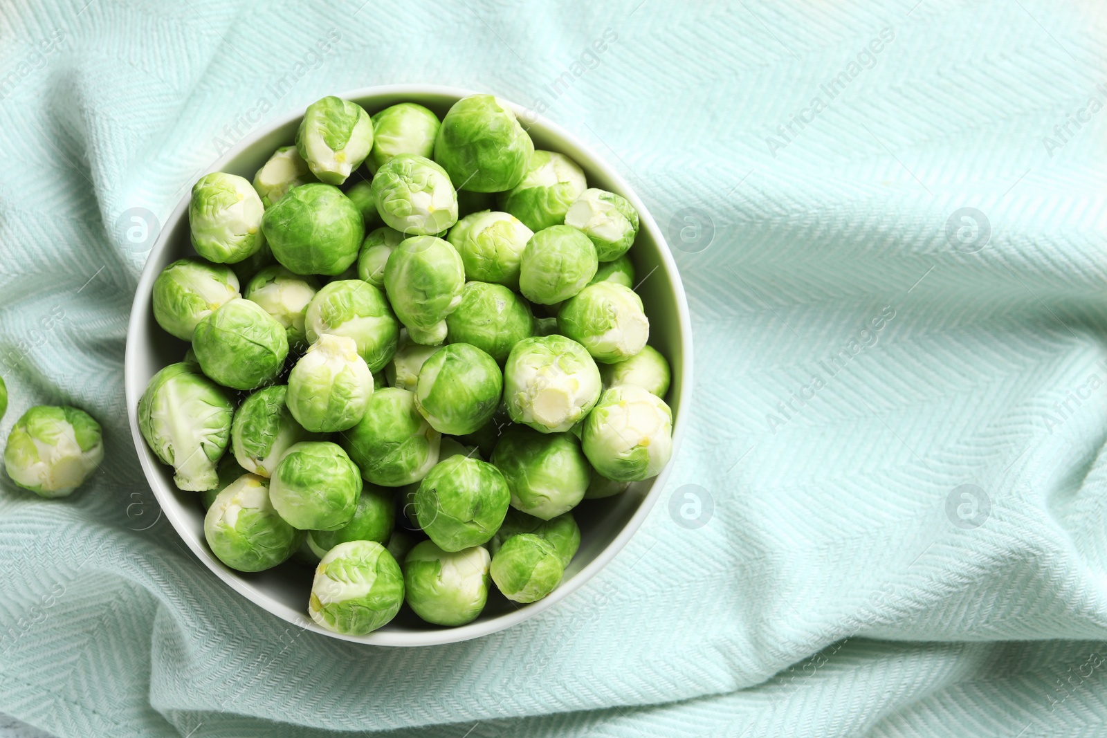 Photo of Bowl of fresh Brussels sprouts on fabric, top view with space for text