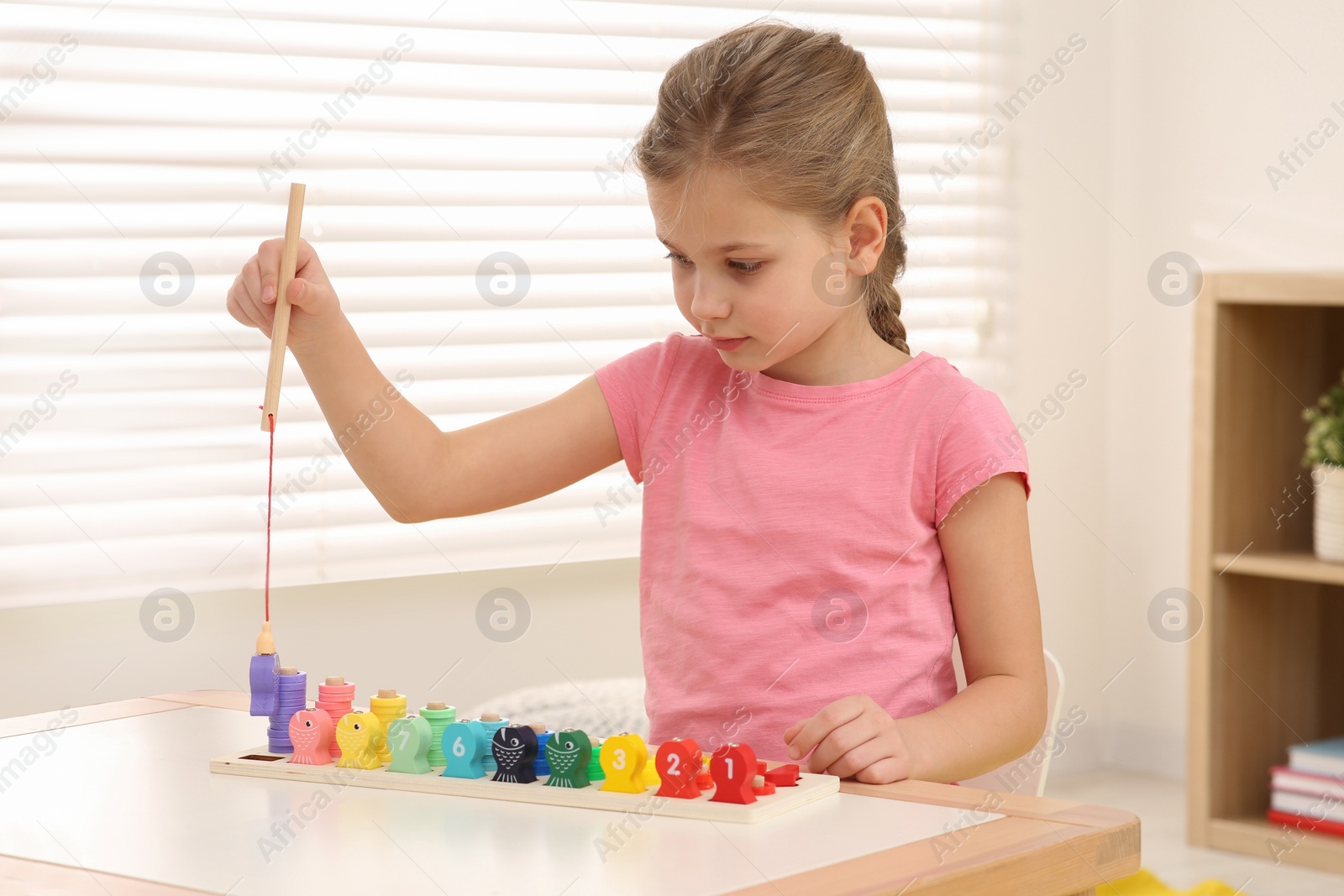 Photo of Little girl playing with Educational game Fishing for Numbers at desk in room. Learning mathematics with fun