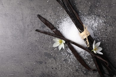 Photo of Vanilla pods, sugar and flowers on gray table, flat lay. Space for text