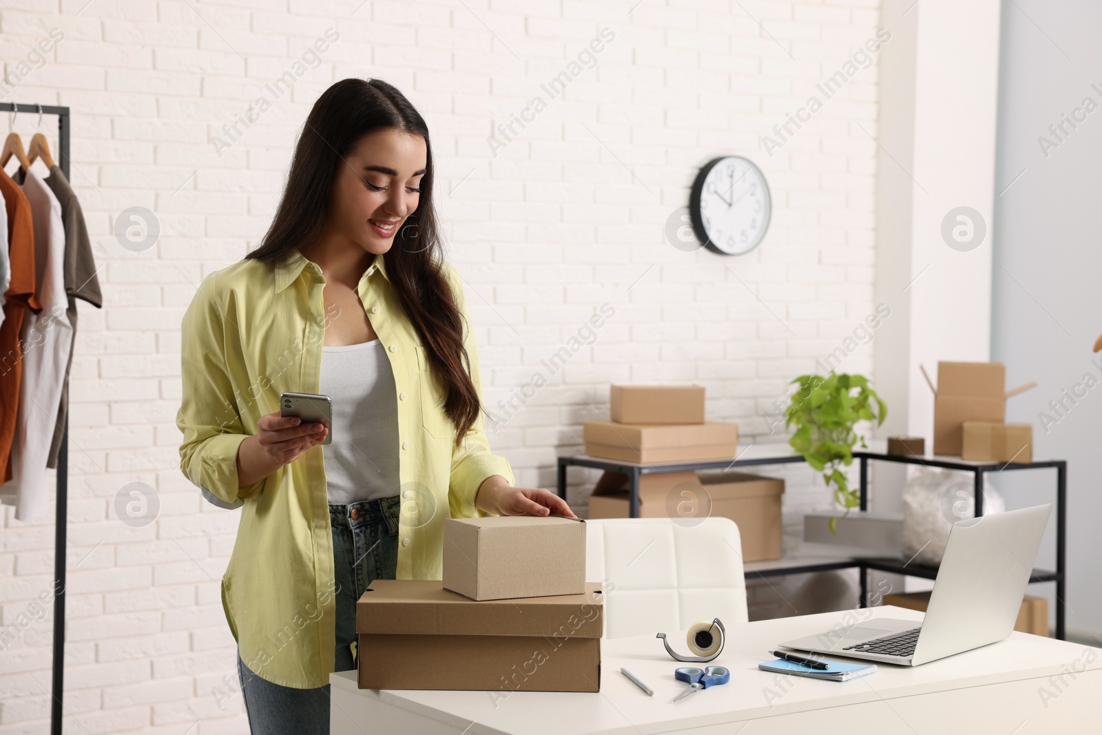 Photo of Seller with laptop, parcels and smartphone in office. Online store