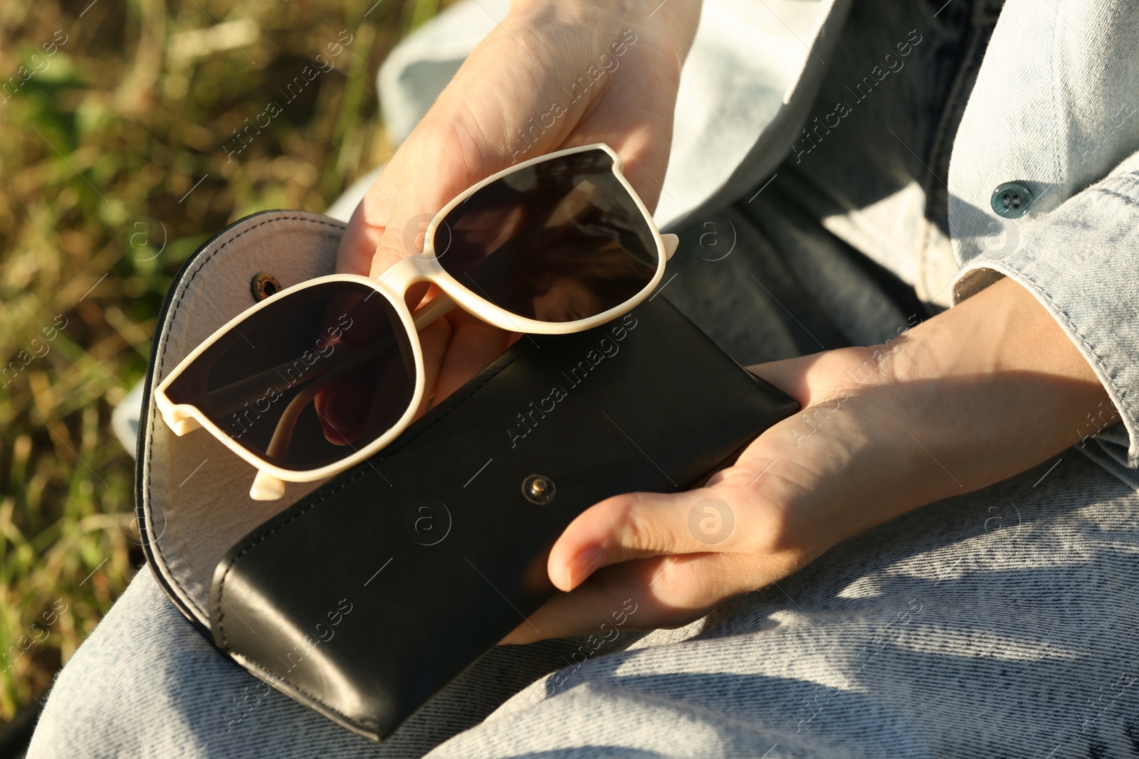 Photo of Woman holding sunglasses and case outdoors on sunny day, closeup