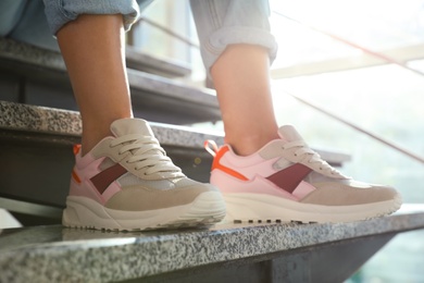 Young woman in stylish sneakers sitting on grey stairs indoors, closeup