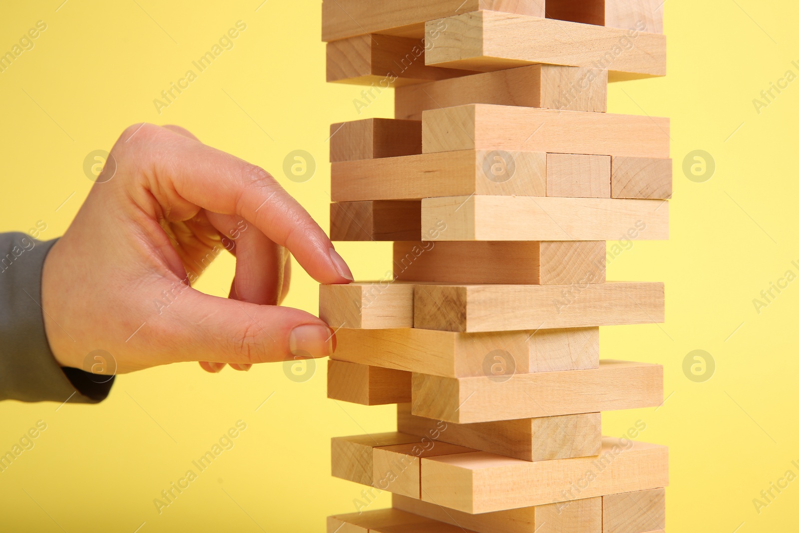 Photo of Woman playing Jenga tower on yellow background, closeup