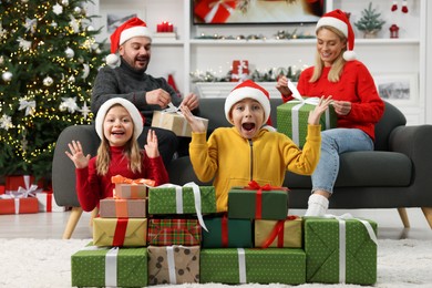 Parents and their surprised children in Santa hats with Christmas gifts at home