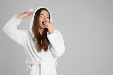 Photo of Beautiful young woman in bathrobe with funny hood  yawning on light grey background. Space for text