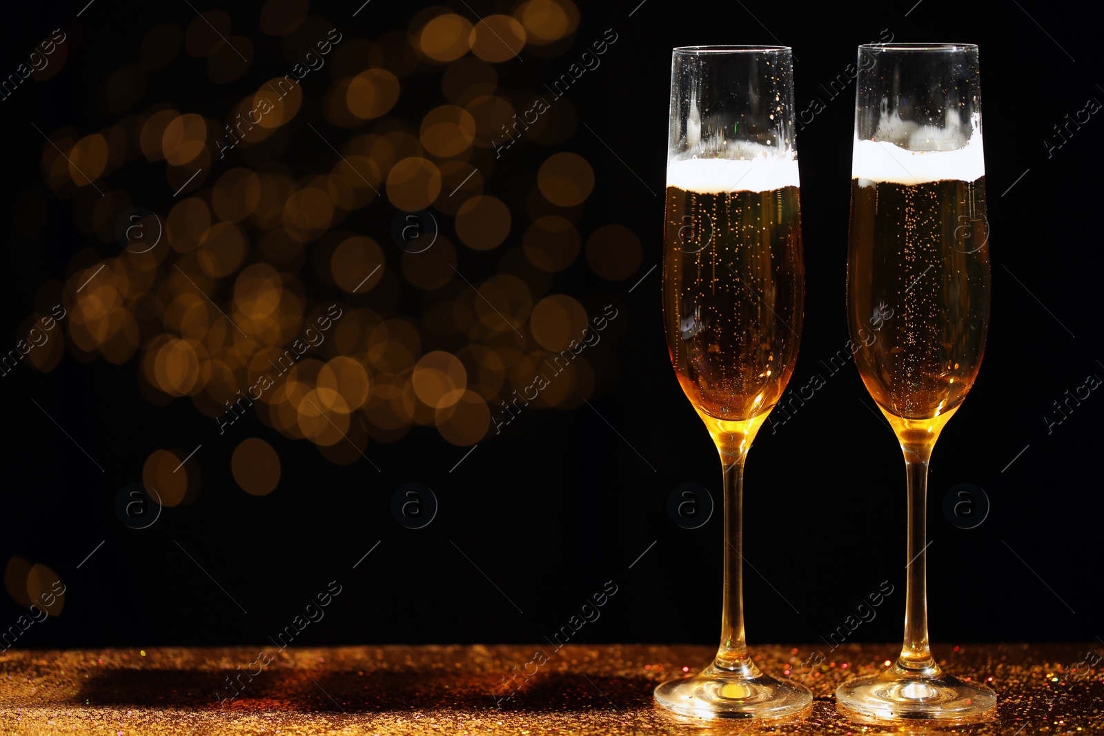 Photo of Glasses of champagne and golden glitter on table against blurred background. Space for text