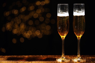 Glasses of champagne and golden glitter on table against blurred background. Space for text