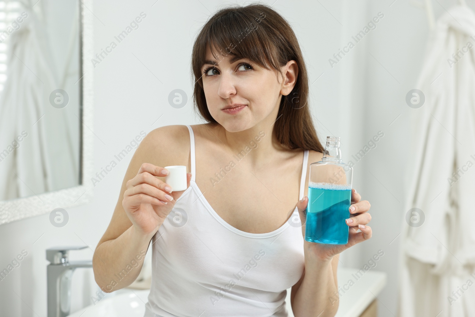 Photo of Young woman using mouthwash in bathroom. Oral hygiene