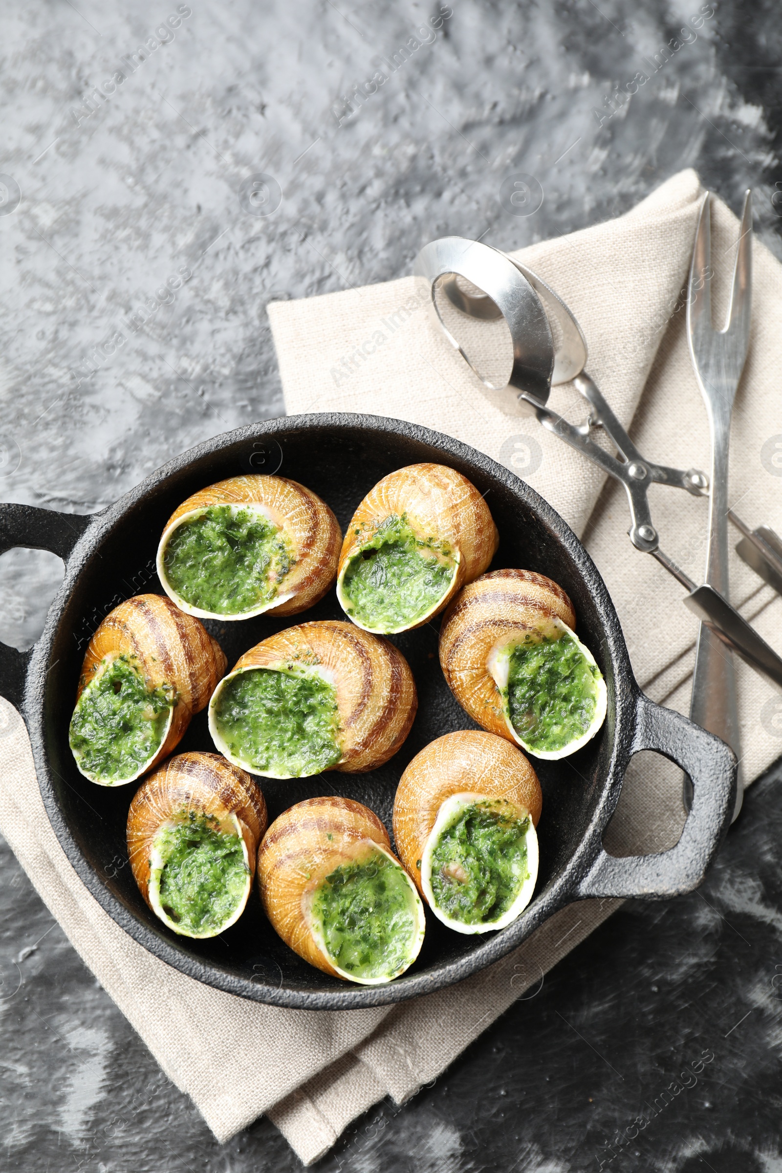 Photo of Delicious cooked snails in baking dish served on grey textured table, flat lay