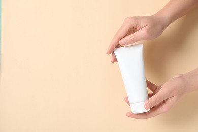 Woman with tube of hand cream on beige background, closeup. Space for text