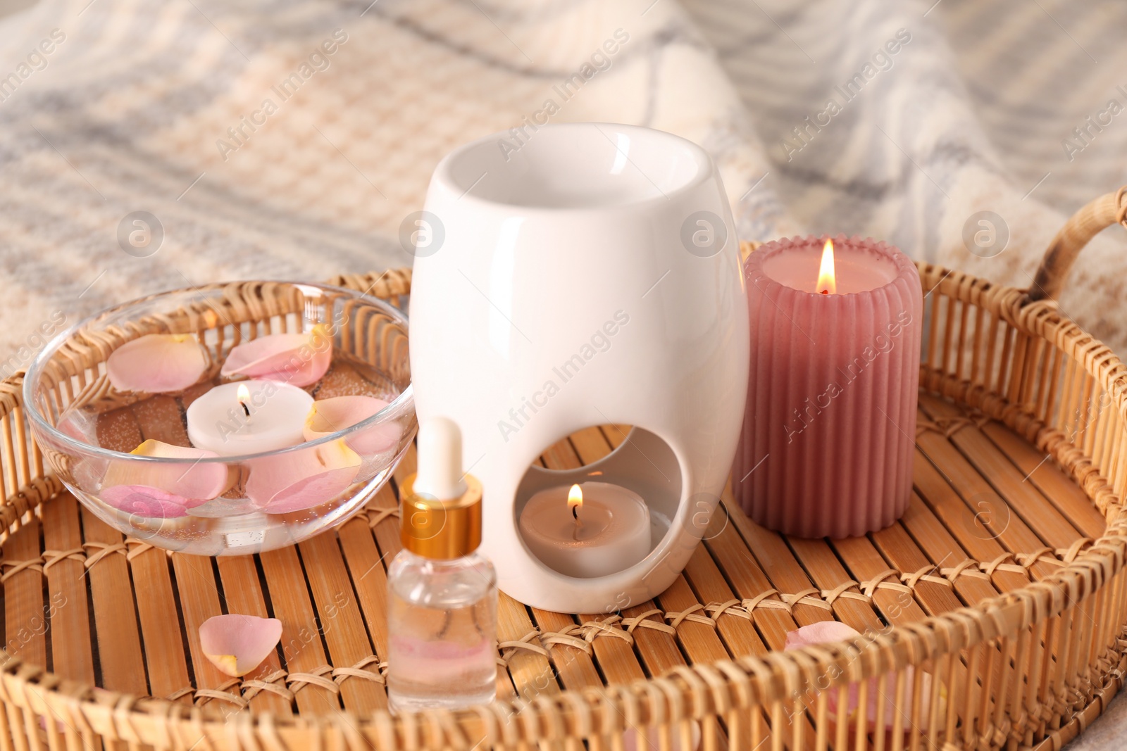 Photo of Wicker tray with aroma lamp, bottle of oil and burning candles on bed