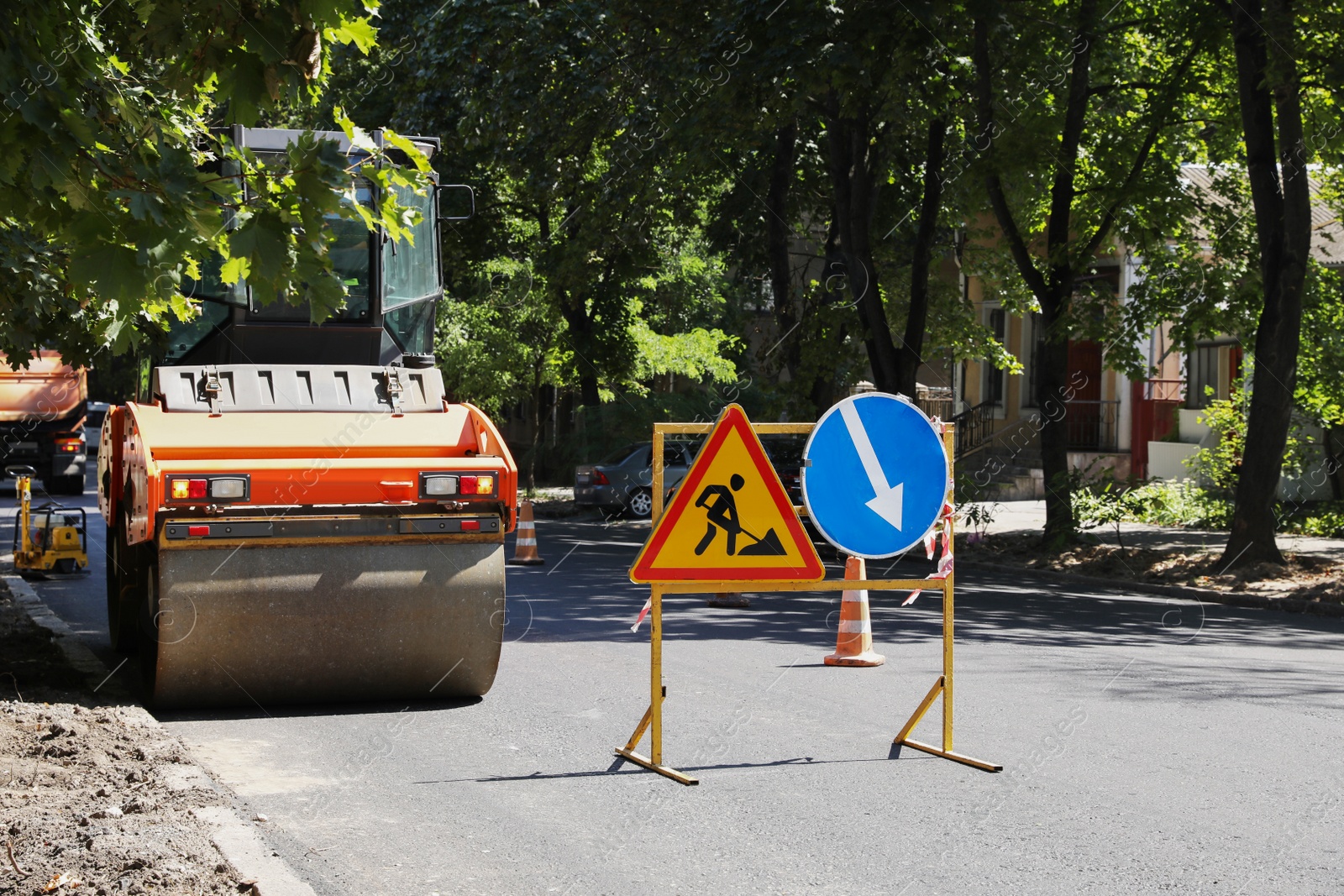 Photo of Roller near barricade with traffic signs on city street. Road repair