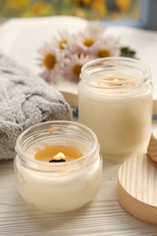 Photo of Burning scented candles, warm sweater and chamomile flowers on white wooden table, closeup