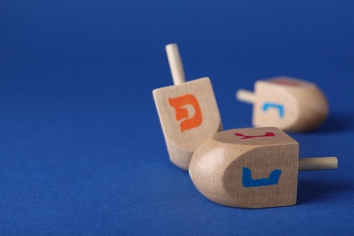 Hanukkah traditional dreidels with letters Pe, Nun and Gimel on blue background, space for text