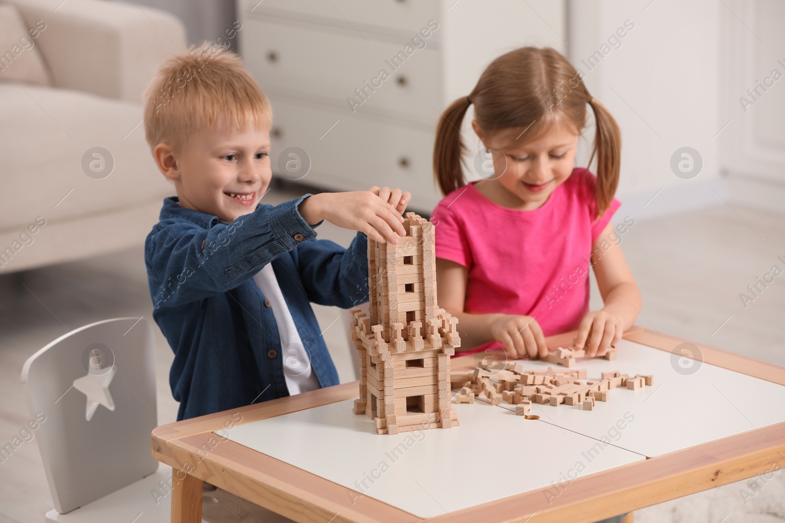 Photo of Little girl and boy playing with wooden tower at table indoors. Children's toy