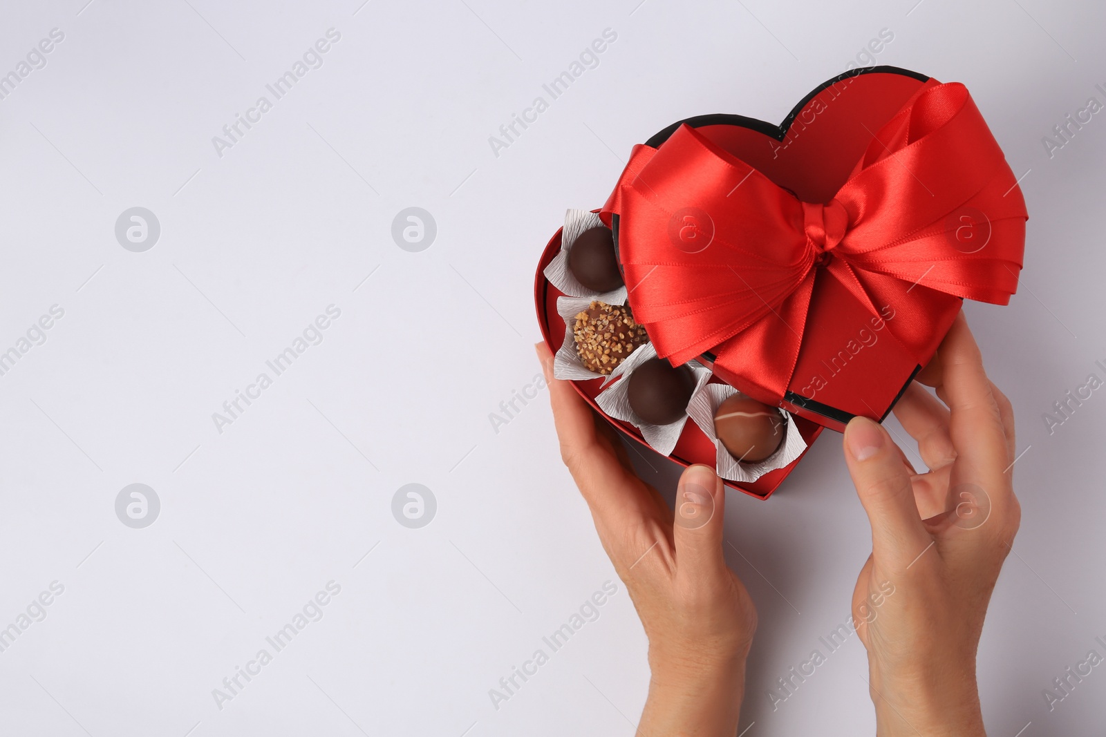 Photo of Woman with box of delicious chocolate candies on white background, top view. Space for text