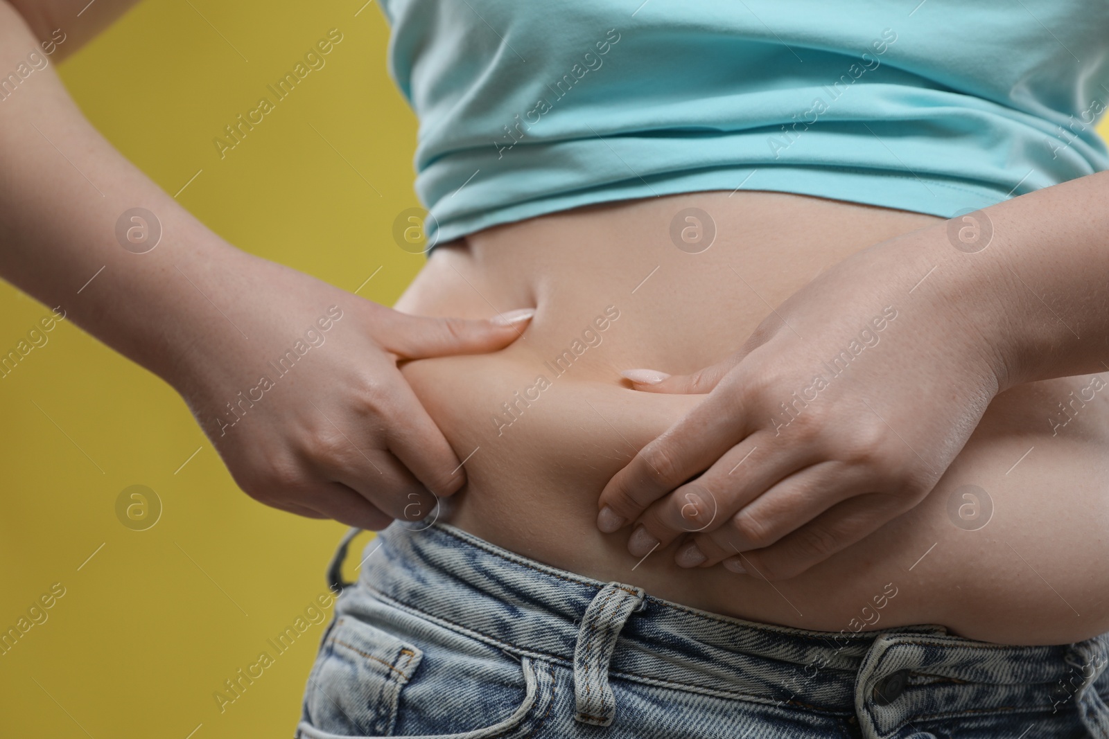 Photo of Woman touching belly fat on yellow background, closeup. Overweight problem