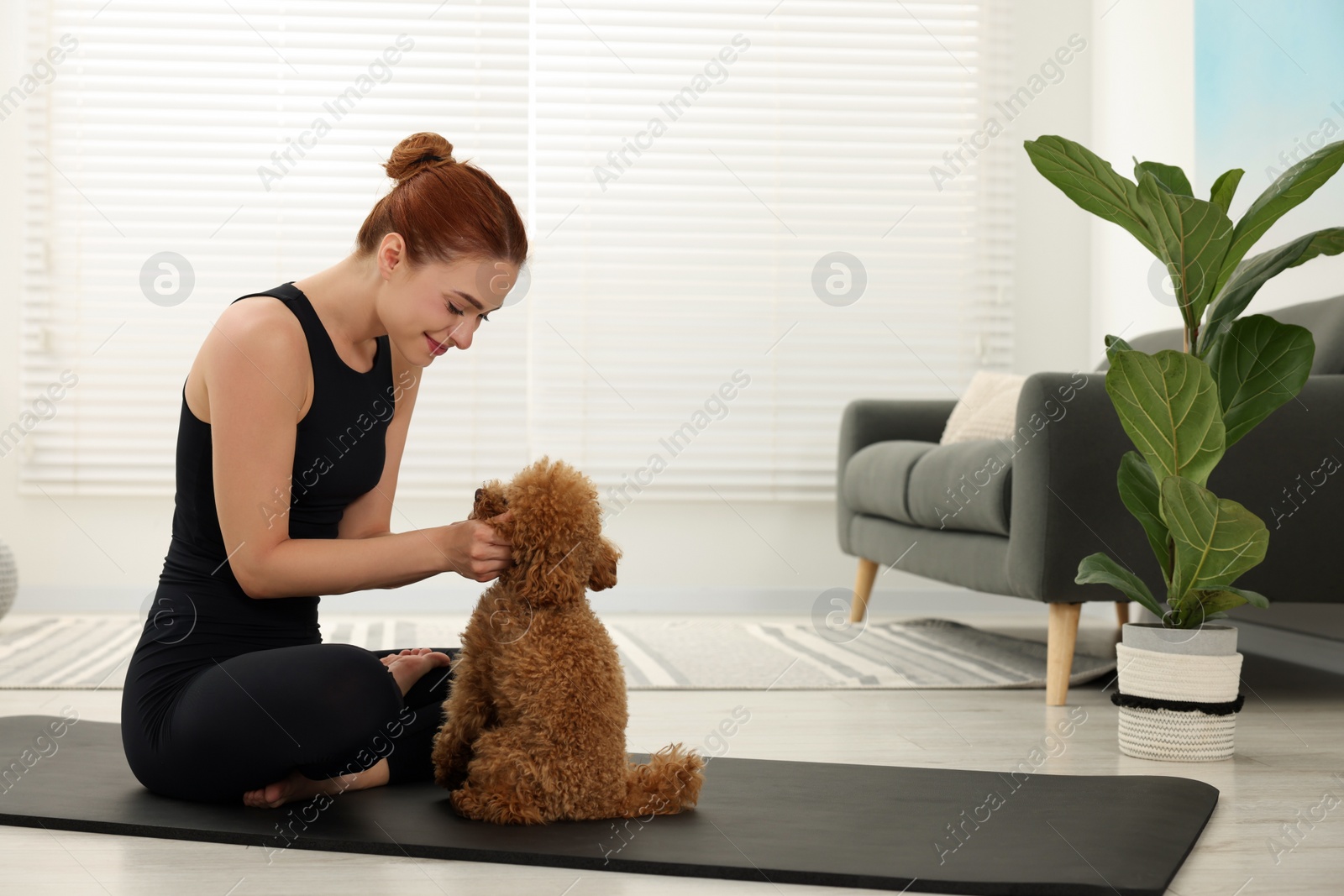 Photo of Young woman practicing yoga on mat with her cute dog at home