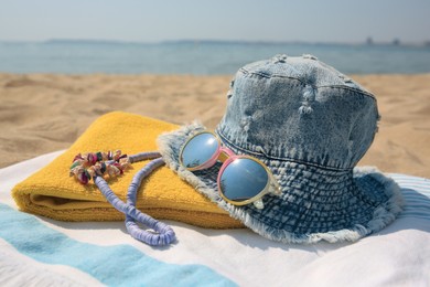 Denim hat and beach accessories on sand near sea, closeup
